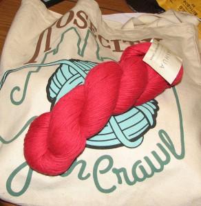 Example skein of the red linen yarn resting on the Rose City Yarn Crawl bag.